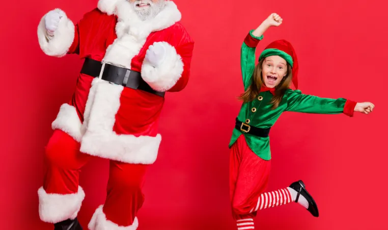 A man dressed as Santa and a girl dressed as an elf dance together with a red background.