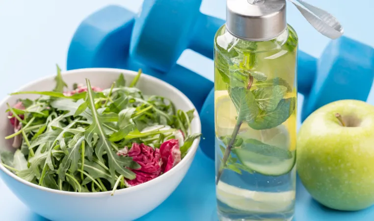 A picture of salad, water, an apple, and weights representing a healthy lifestyle.