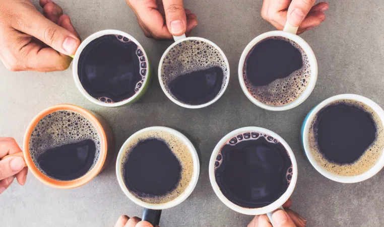 A group of people's hands hold cups of coffee together.