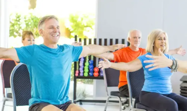 A group of older adults participate in a group chair exercise class.
