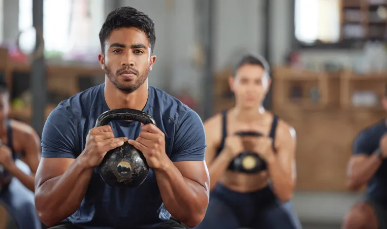 A group of people squat with kettlebells during a group exercise class.
