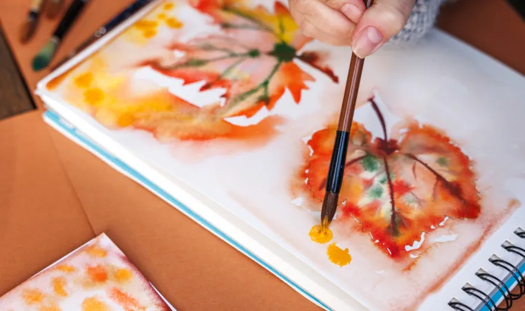 A close up of someone painting watercolor leaves.
