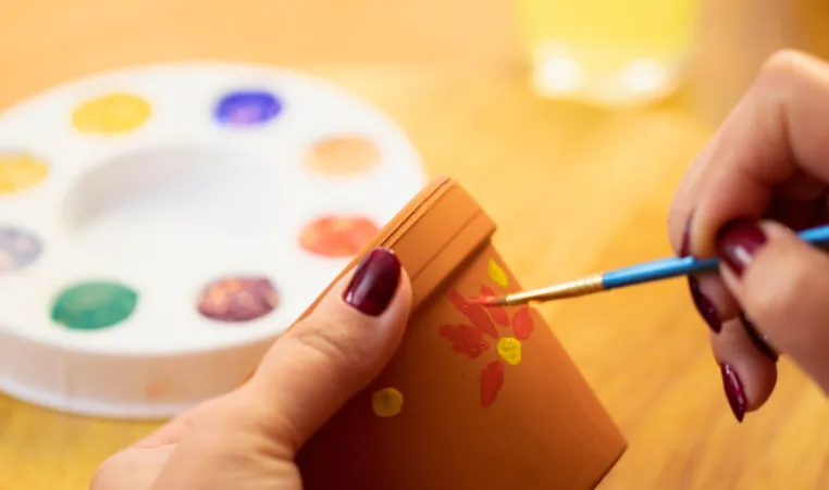 A pair of hands paint a flowerpot.