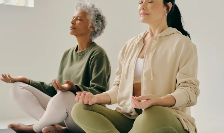 Two women sit on the floor in a yoga pose during a class.