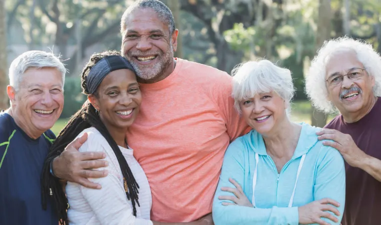 A group of older adults smile and embrace each other outside.