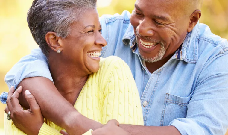 An older couple embrace and smile at each other as they sit outside.
