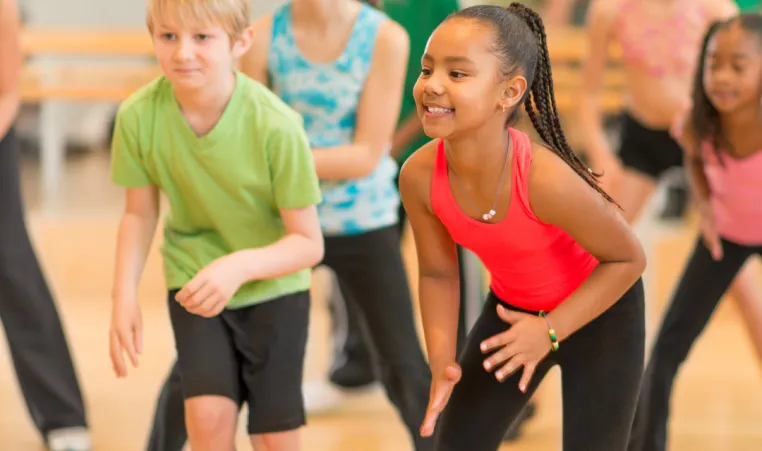 A group of kids smile and dance during a group dance class.