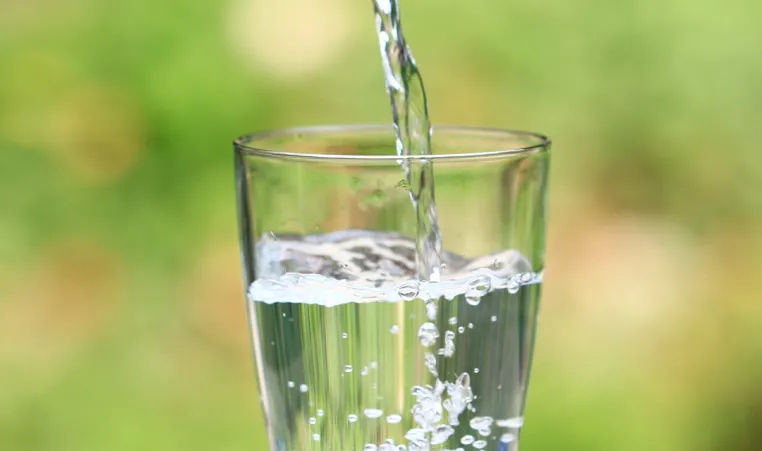 A glass sitting on a table outside being filled with water.