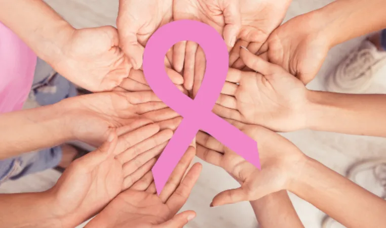 A group of hands hold a pink Breast Cancer Awareness ribbon.