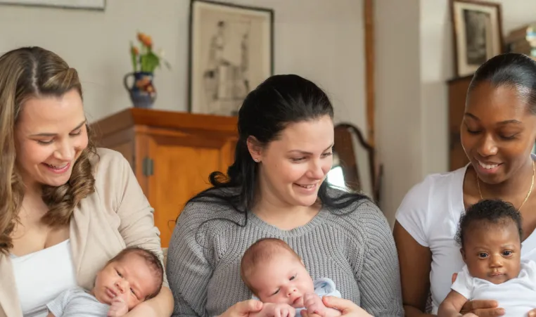Three mothers with babies sit together in a postpartum support group.