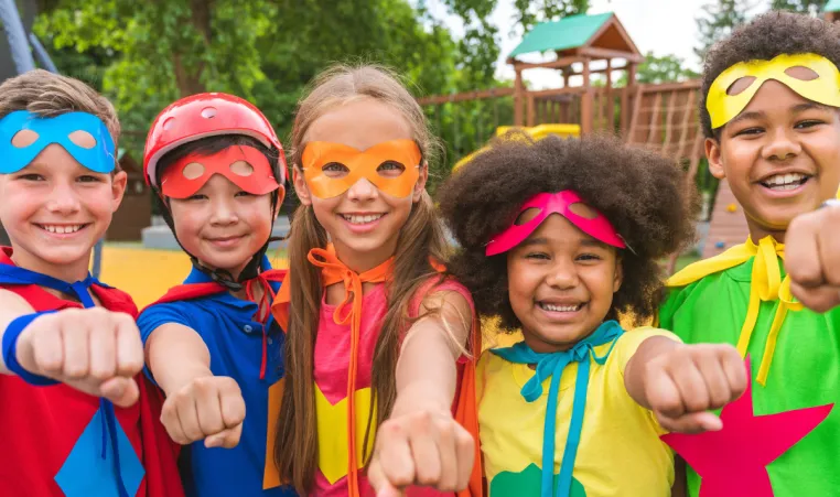 A group of kids dressed as superheroes smile and play outside.
