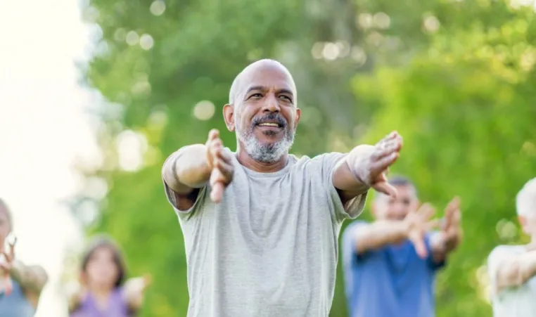 A group of older adults participate in a tai chi group exercise class outside.