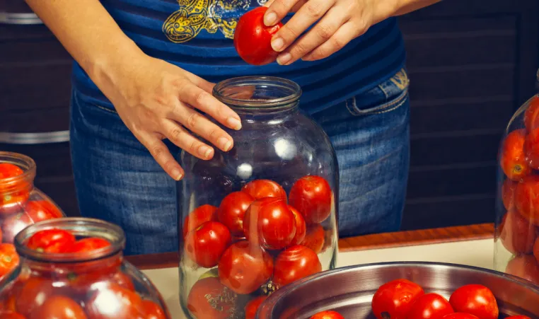 Close-up of a woman canning tomatoes in jar to preserve them.