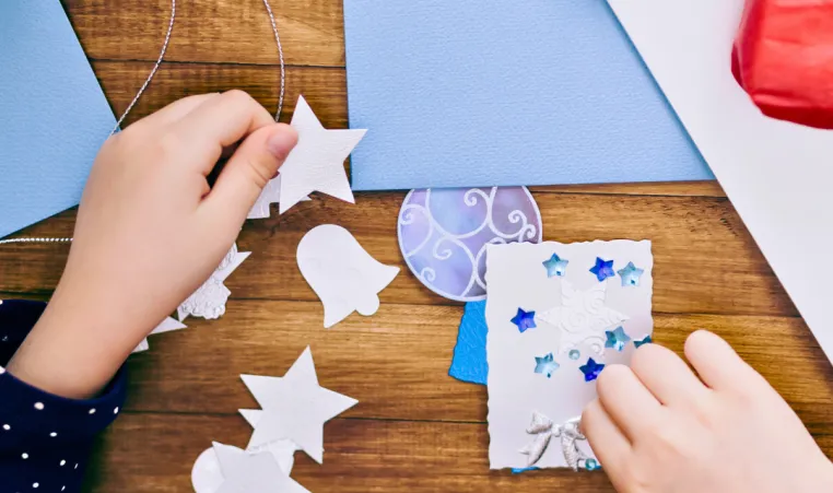 Close-up of hands making winter holiday card crafts.